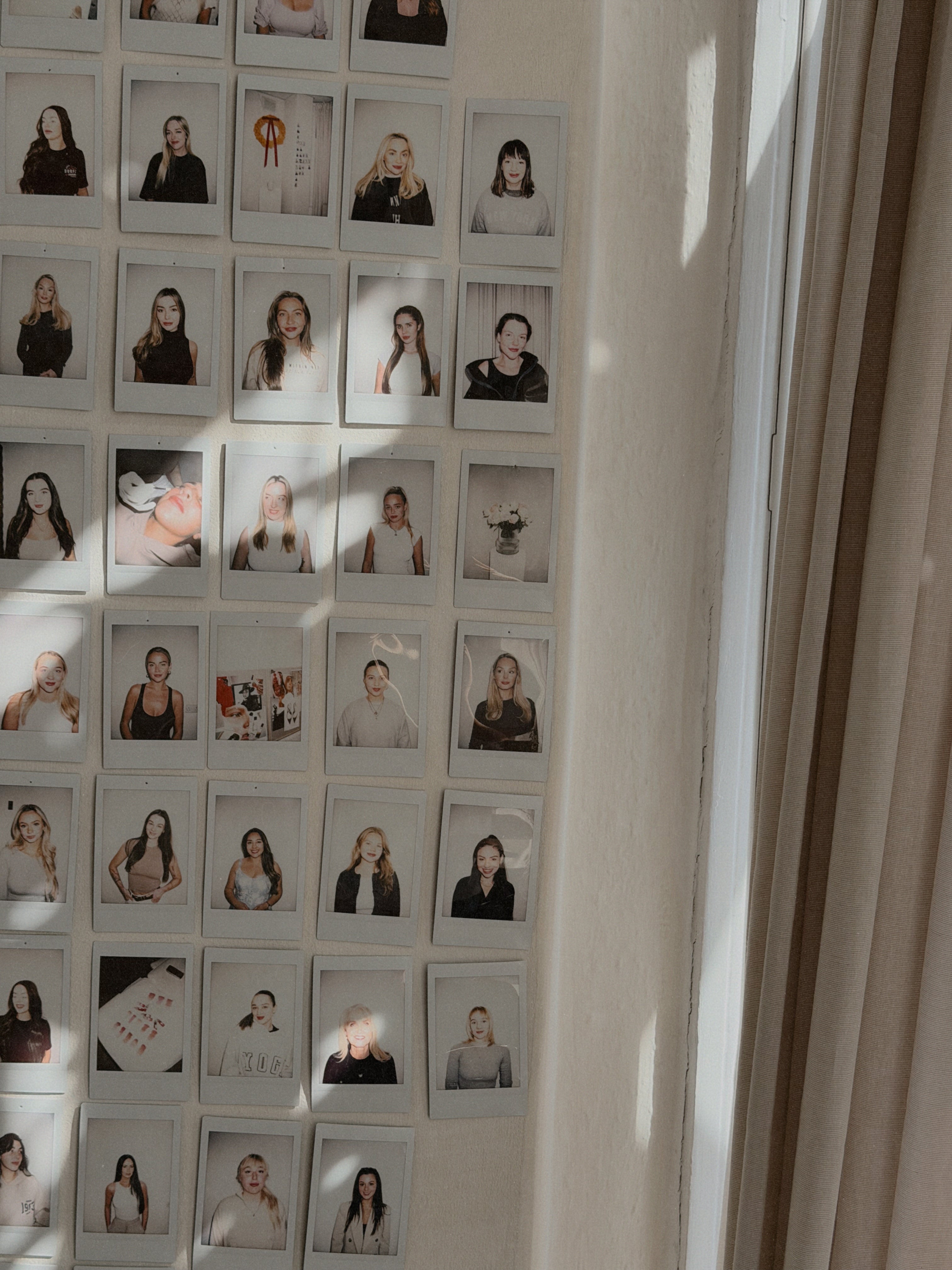 Grid of small photographs on a wall with a light fixture above.